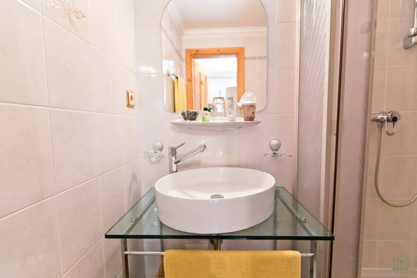 Modernes Badezimmer mit Aufsatzwaschbecken auf Glasplatte und weißer Fliesenwand.