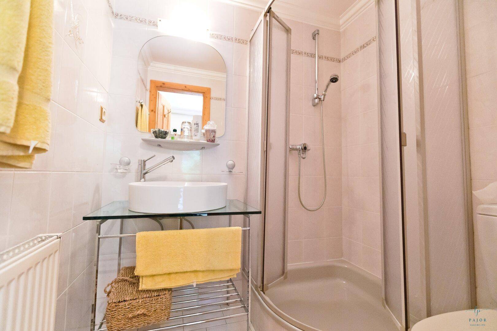 Helles Badezimmer mit Duschkabine, Aufsatzwaschbecken und weißen Fliesen.