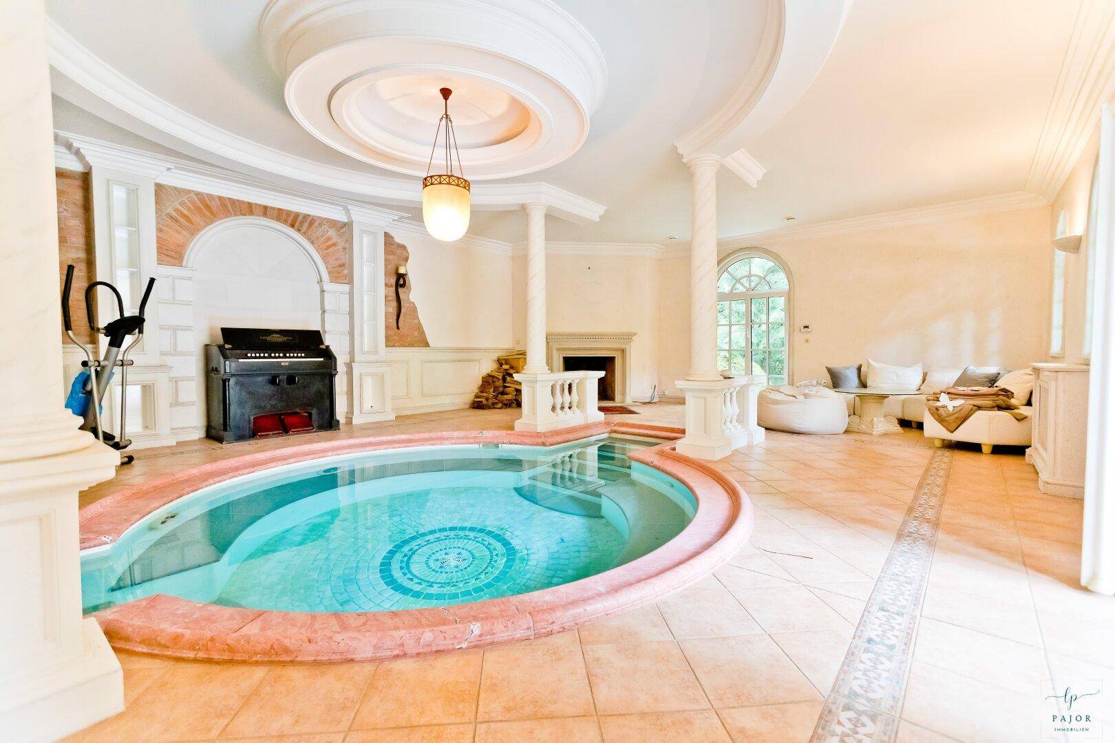 Luxuriöser Wellnessbereich mit Innenpool, Sitzgelegenheiten und Blick in den Garten.