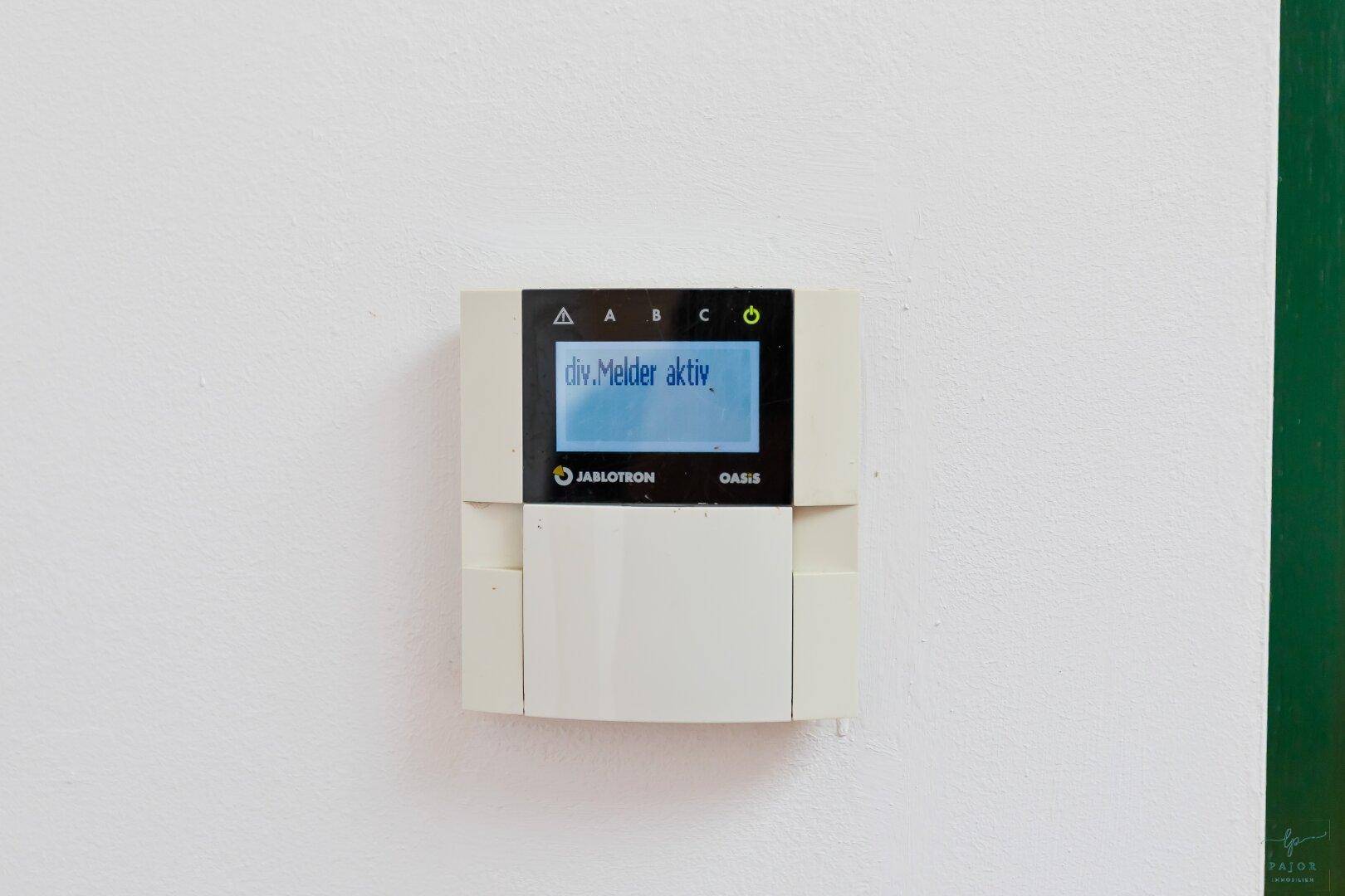 Ein Jablotron Oasis Sicherheitssystem-Bedienfeld an einer weißen Wand.
