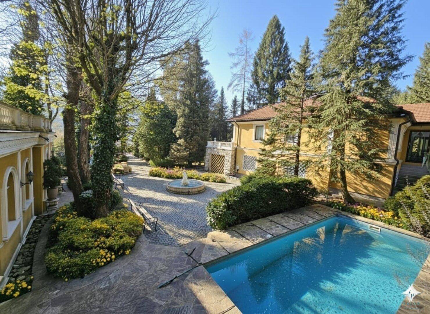 Weitläufiges Anwesen mit Pool, Springbrunnen und gepflegter Gartenanlage unter blauem Himmel.