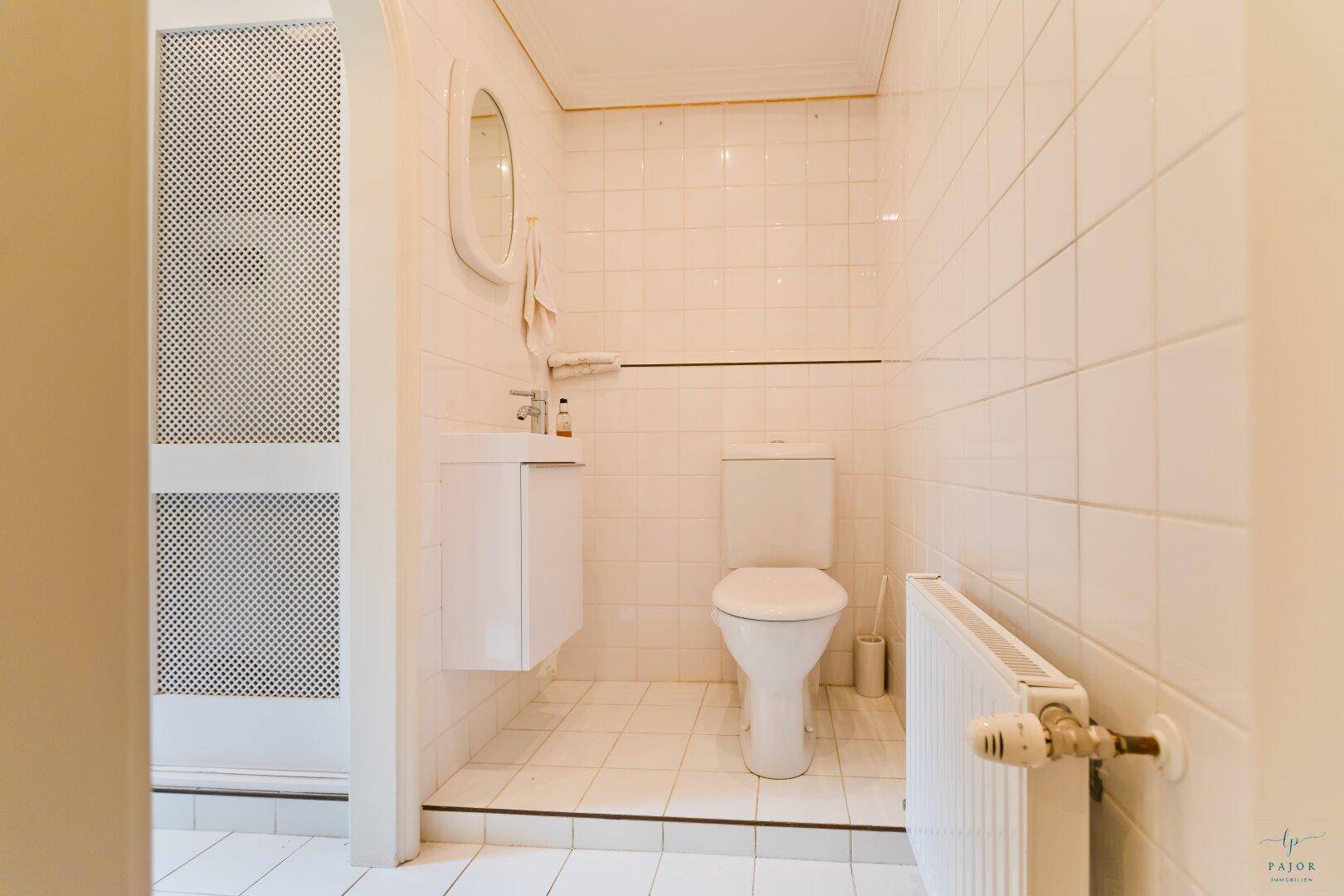 Kleines WC mit weiß gefliesten Wänden, Hänge-Waschbecken und Heizkörper.