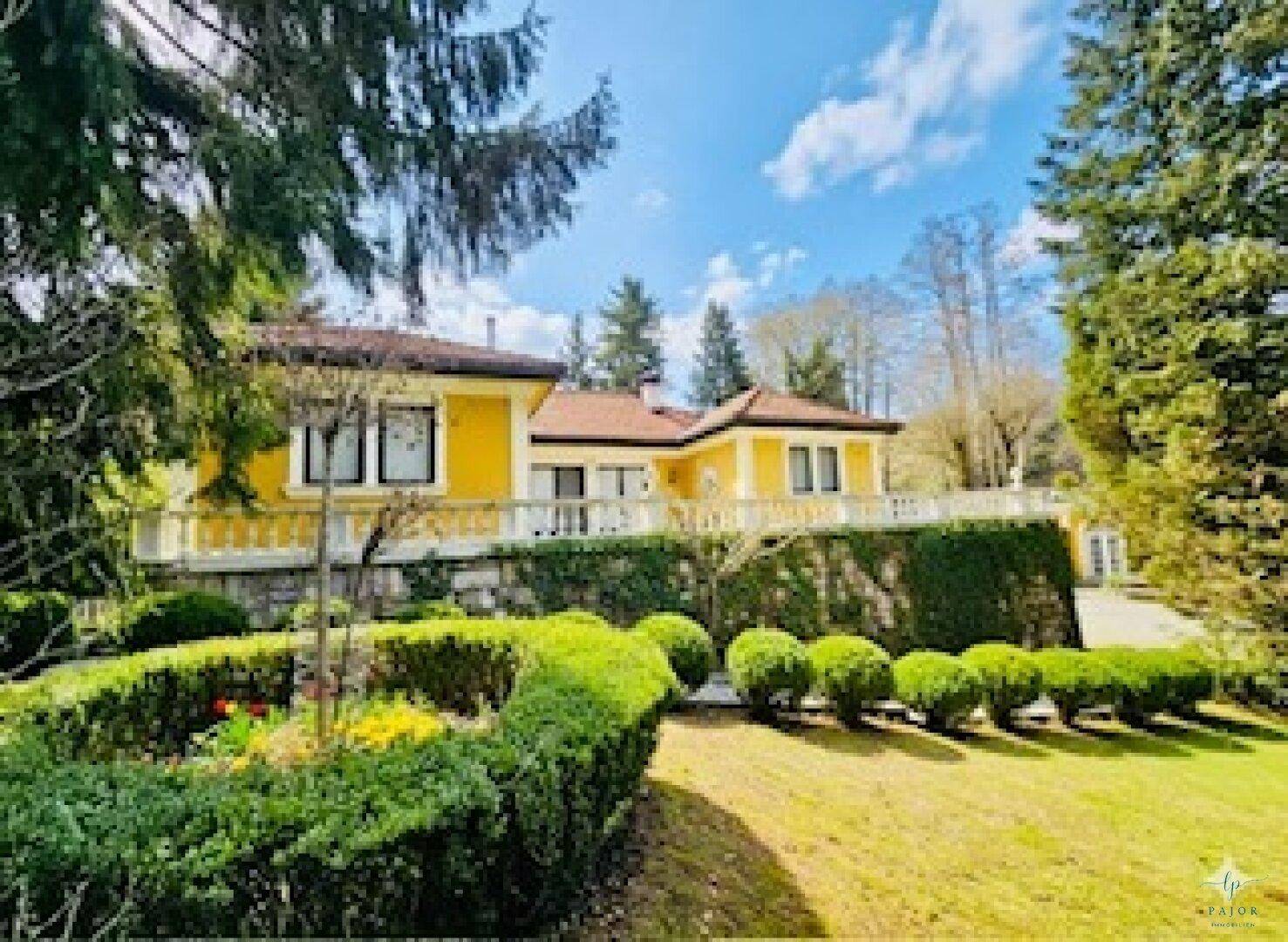 Die gelbe Villa mit gepflegtem Garten und grünen Hecken unter blauem Himmel.