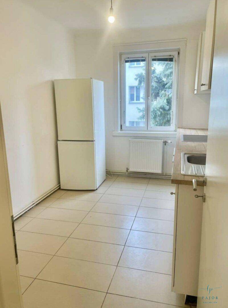 Helle Küche mit Fliesenboden, weißem Kühlschrank und Fenster, bietet Potenzial für eine moderne Einrichtung.