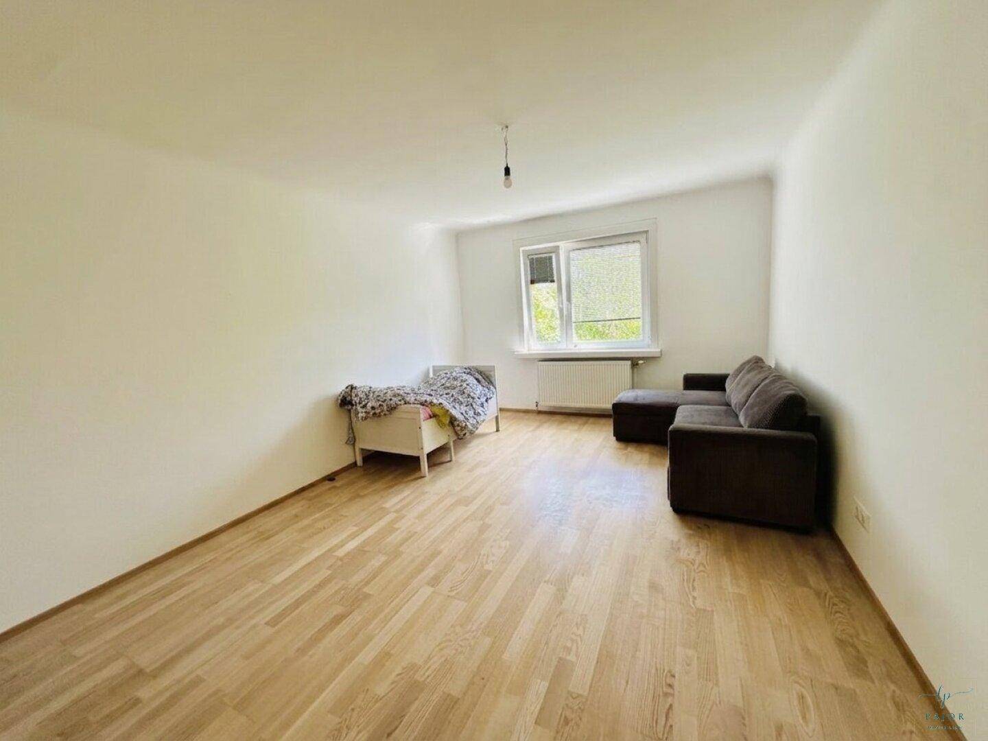 Gemütliches Wohnzimmer mit Parkettboden, einem Sofa und einem kleinen Bett, ideal zum Entspannen.