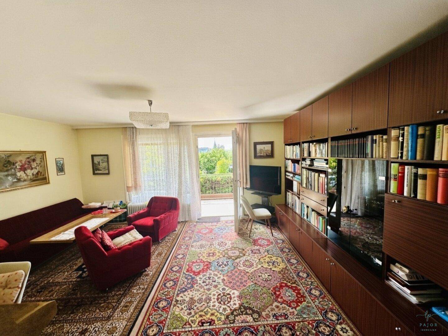 Geräumiges Wohnzimmer mit großer Bücherwand, traditionellen Möbeln und direktem Zugang zum Balkon.