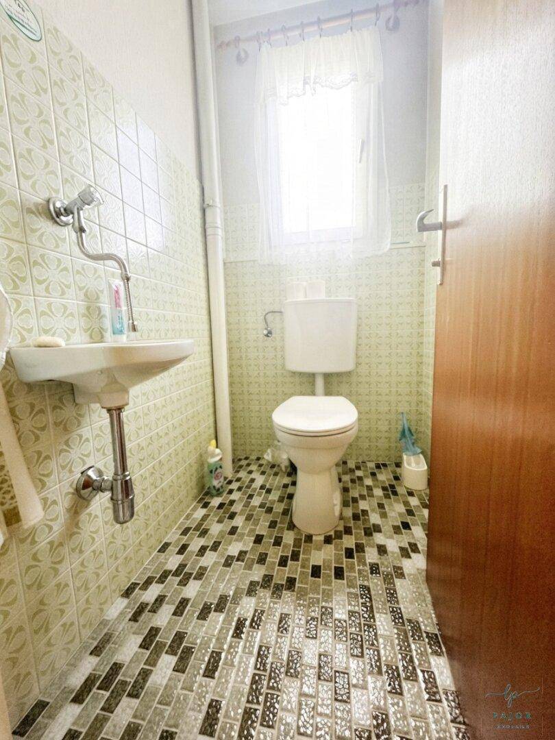 Kleines Gäste-WC mit gemusterten Fliesen, Waschbecken und Toilette, hell durch ein kleines Fenster.