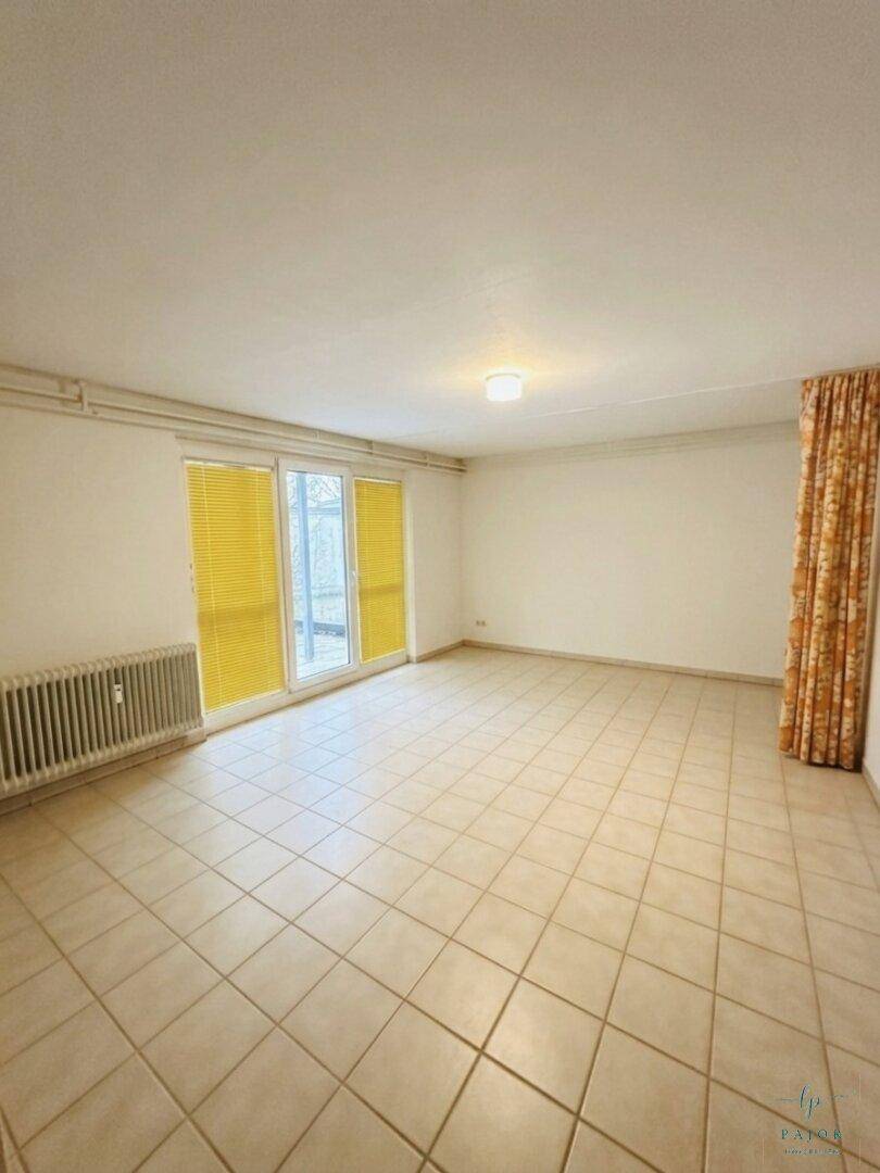 Geräumiges, leeres Zimmer mit Fliesenboden und großer Schiebetür, die viel Licht hereinlässt.