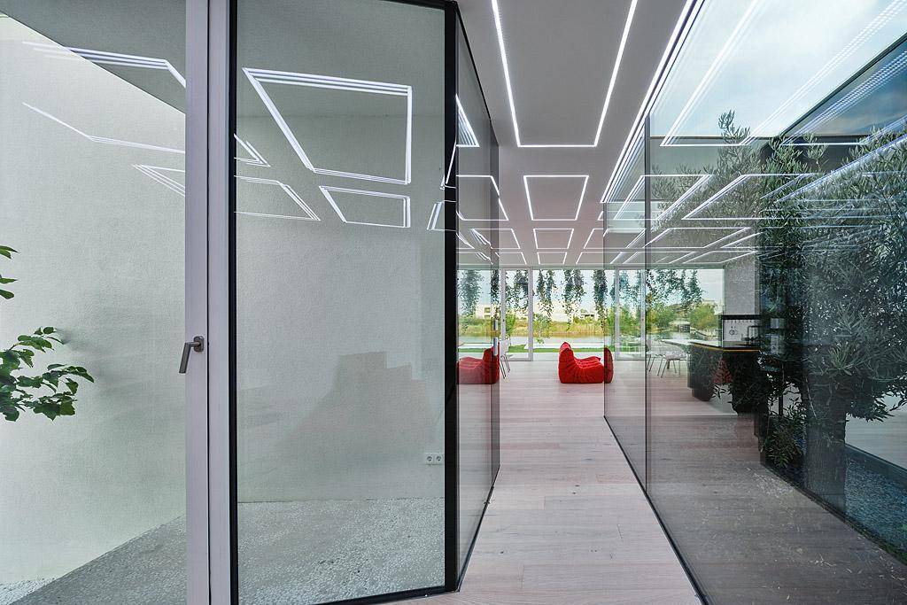 Moderner Wohnbereich mit großen Glasfronten, Holzboden und indirekter Deckenbeleuchtung.