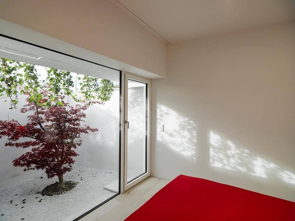 Schlafzimmer mit minimalistischem Design, rotem Bett und direktem Blick auf einen begrünten Innenhof.