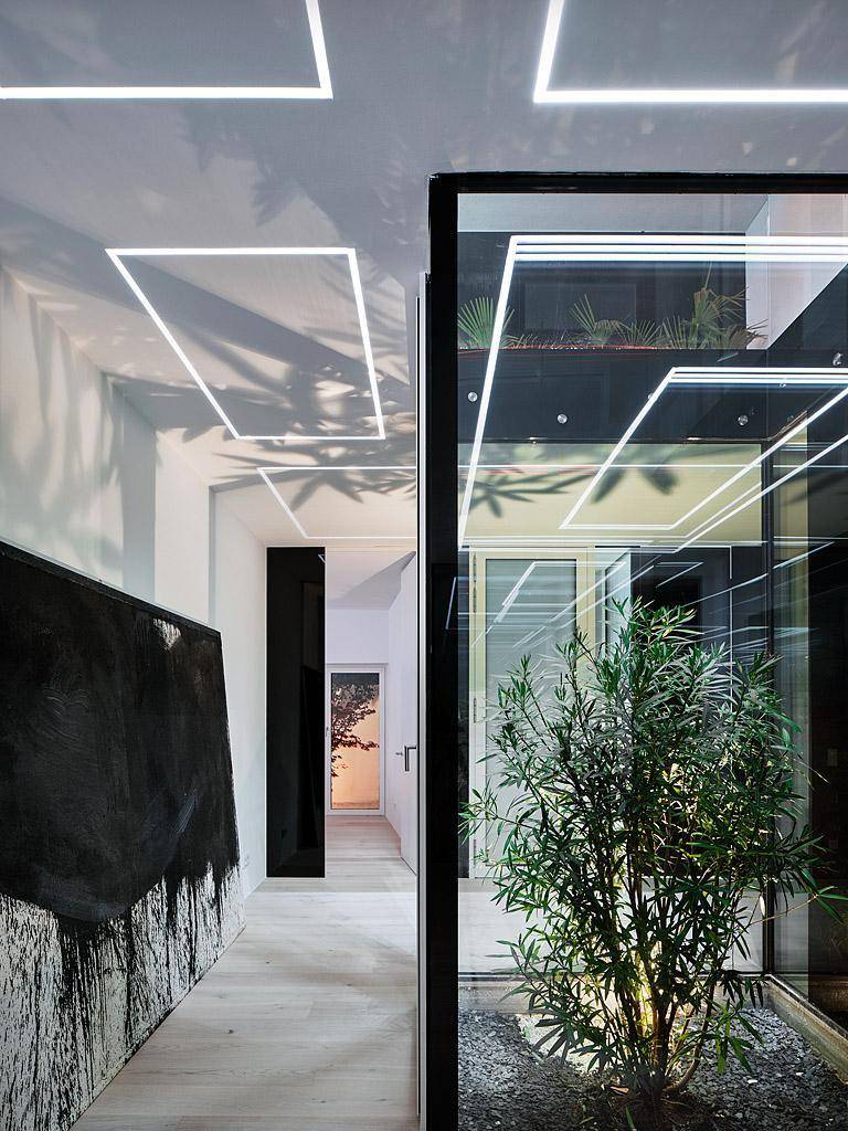 Moderner Flur mit Kunstwerk, Holzboden und Blick auf einen begrünten Innenhof.