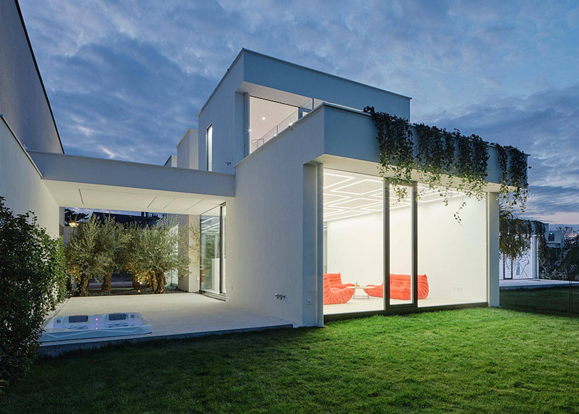 Gartenbereich der modernen Villa bei Dämmerung mit Rasenfläche und Whirlpool.