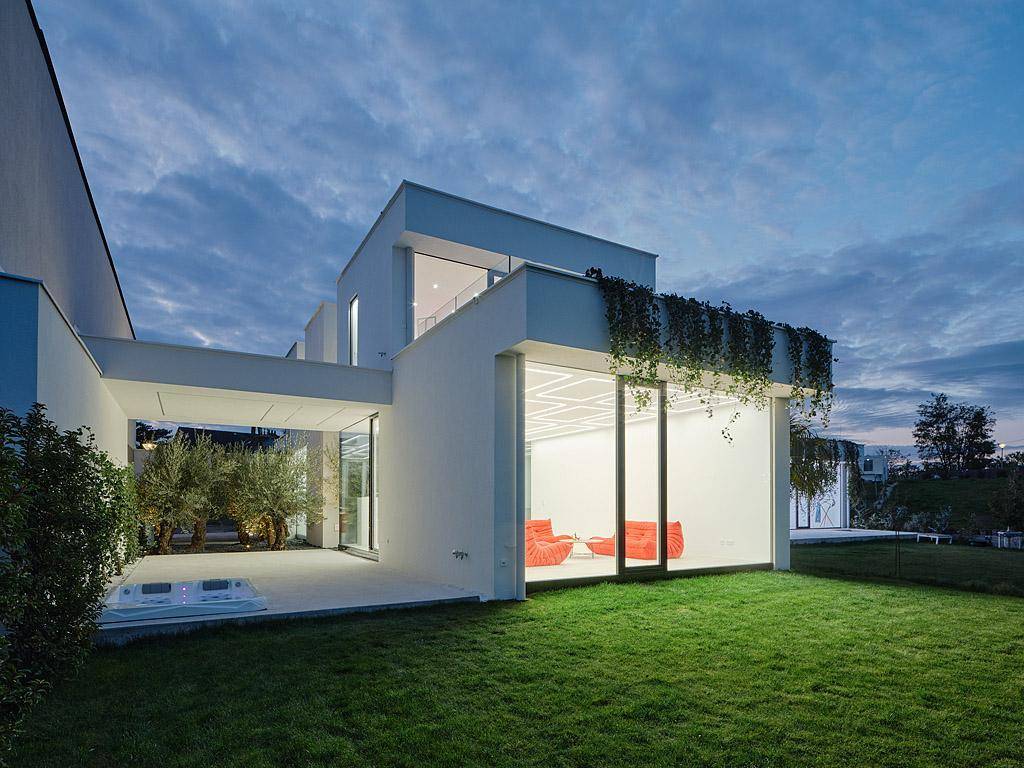 Gartenbereich der Villa in der Abenddämmerung mit Rasenfläche, Whirlpool und beleuchteten Innenräumen.