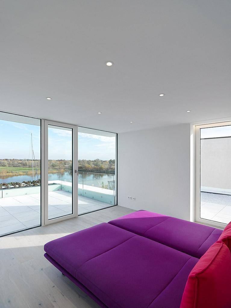 Helles Schlafzimmer mit Seeblick, Holzboden und großen Schiebetüren zur Terrasse.