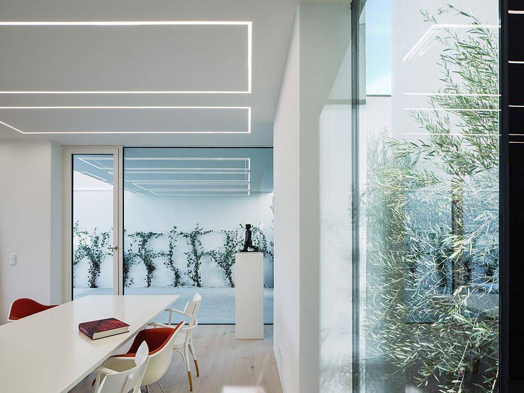 Essbereich mit minimalistischem Design, Holzboden und Blick auf einen begrünten Innenhof.