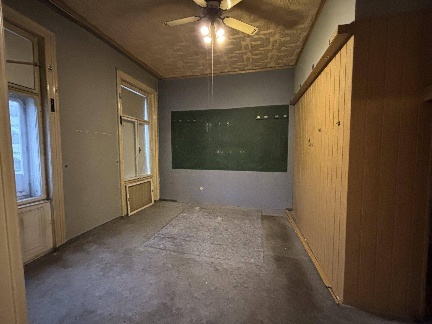 Raum in Renovierungszustand mit alten Fenstern und Holzverkleidung an der Wand.