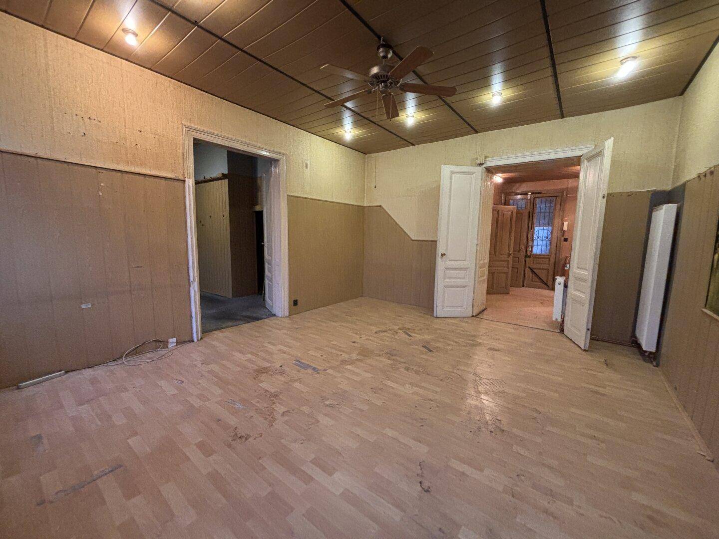 Großes Wohnzimmer mit Deckenventilator, Holzboden und Renovierungsbedarf.