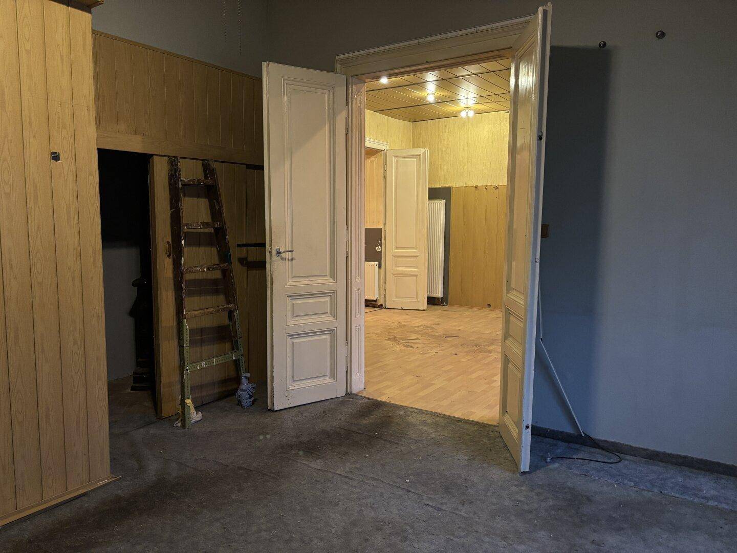 Raum in Renovierungszustand mit alten Holztüren und abgenutztem Boden.