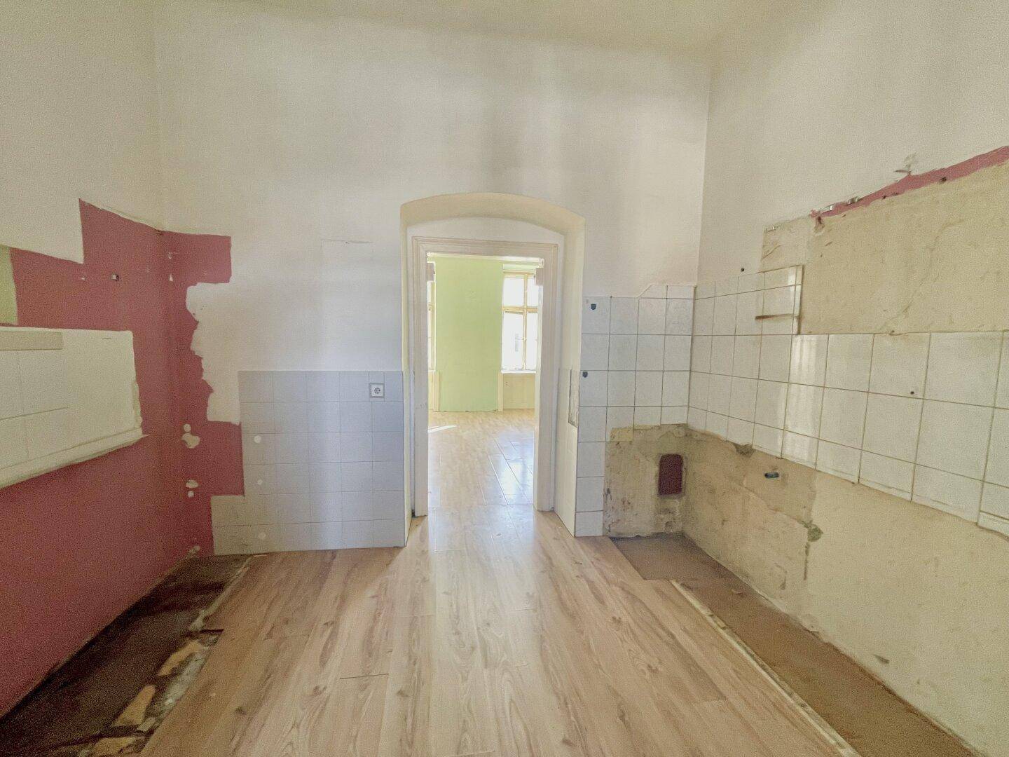 Leere Küche mit alten Fliesen, Holzboden und einem Durchgang zu einem weiteren Zimmer.