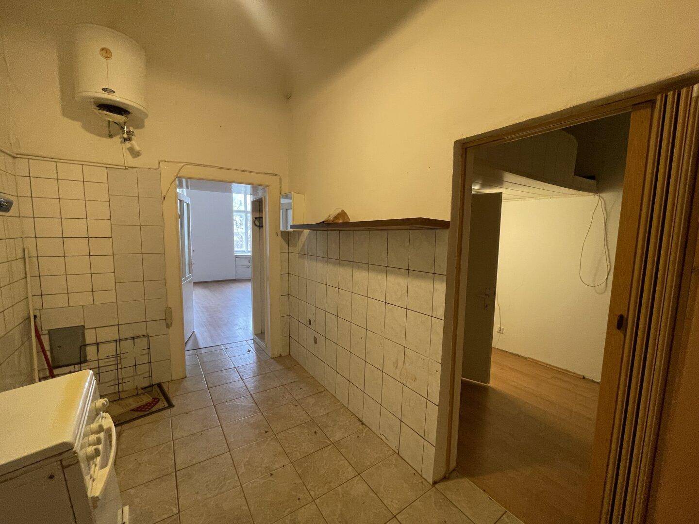 Einfache Küche in Originalzustand mit Fliesenboden und Wandfliesen, inklusive Herd und Boiler.