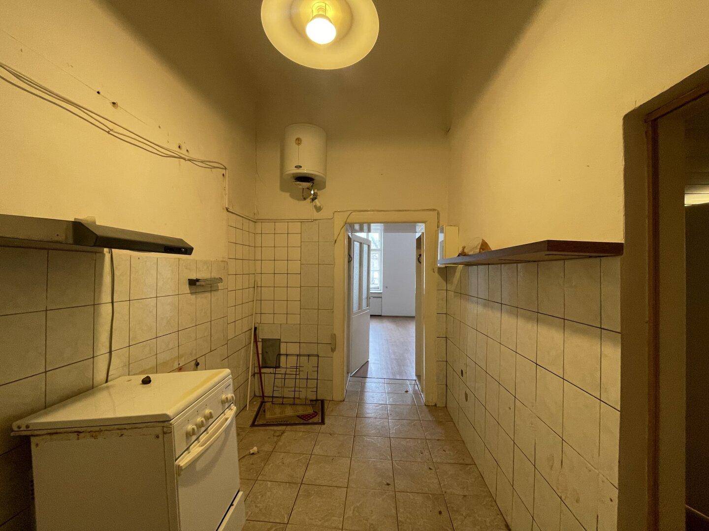 Küche in Originalzustand mit Fliesenboden, Wandfliesen und einem einfachen Herd, funktional und schlicht.