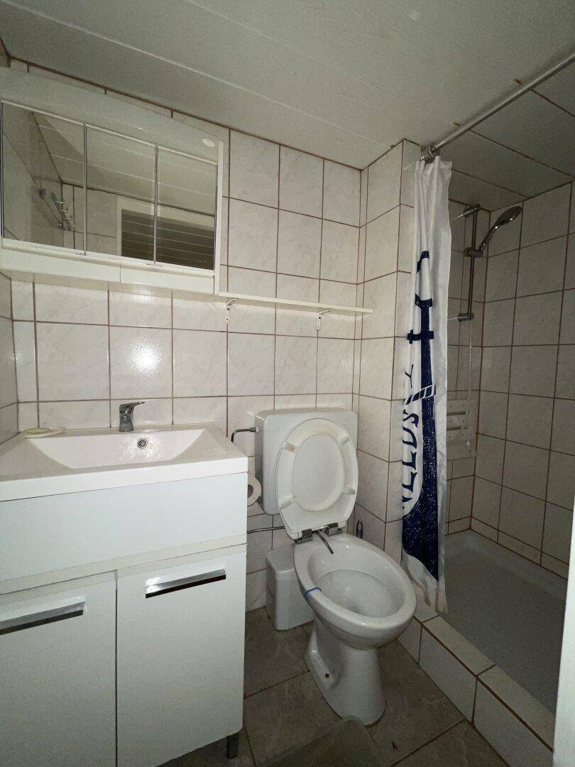 Badezimmer in Originalzustand mit Dusche, WC, Waschbecken und Spiegelschrank, komplett gefliest.