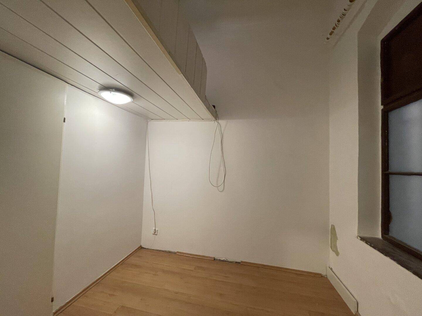 Kleiner Raum mit Holzboden, Fenster und einer eingebauten Loft-Struktur, die zusätzlichen Platz schafft.