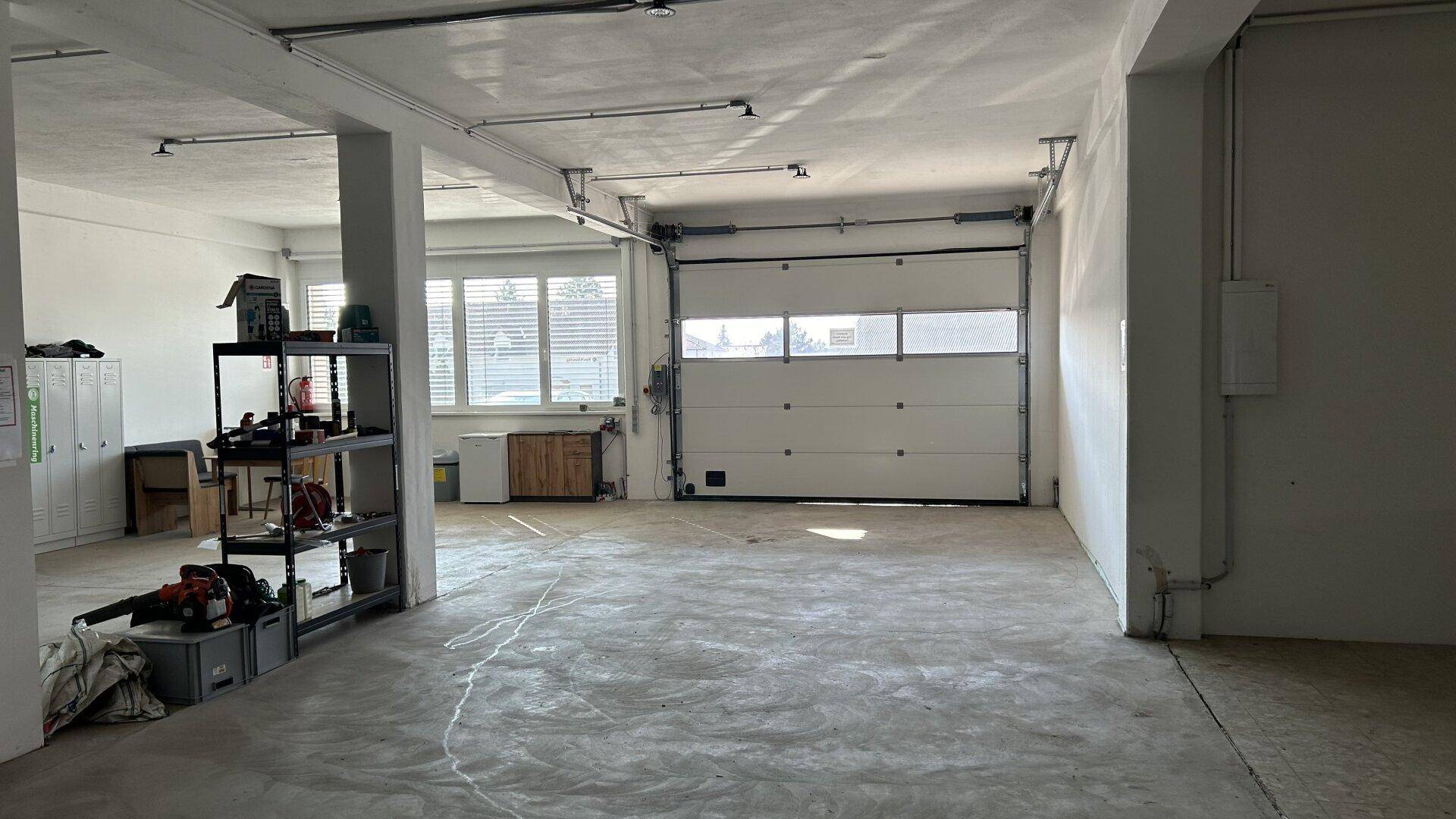 Geräumige Garage mit Rolltor und Fenstern, bietet viel Platz für Fahrzeuge oder Lagerung.