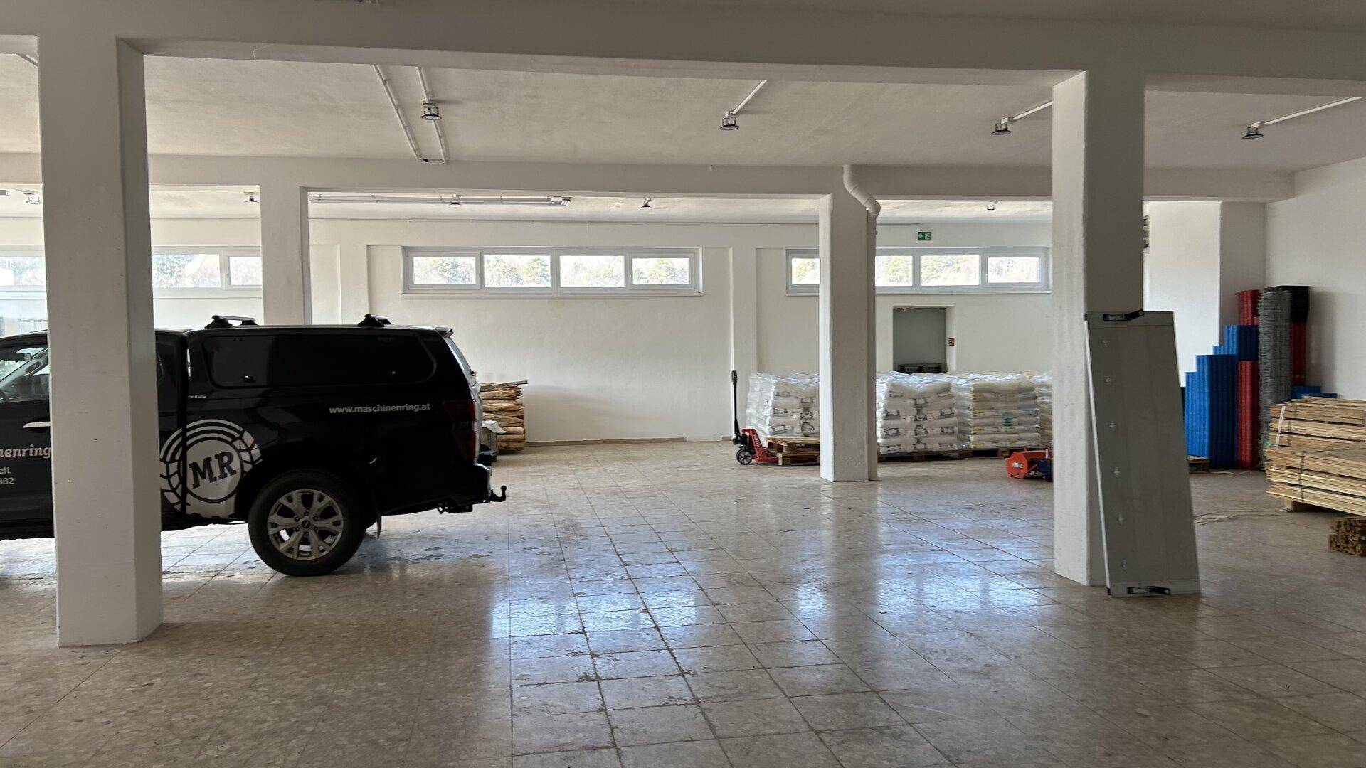 Großer Raum mit Fliesenboden, Säulen und einem geparkten Fahrzeug, genutzt als Lager oder Arbeitsbereich.