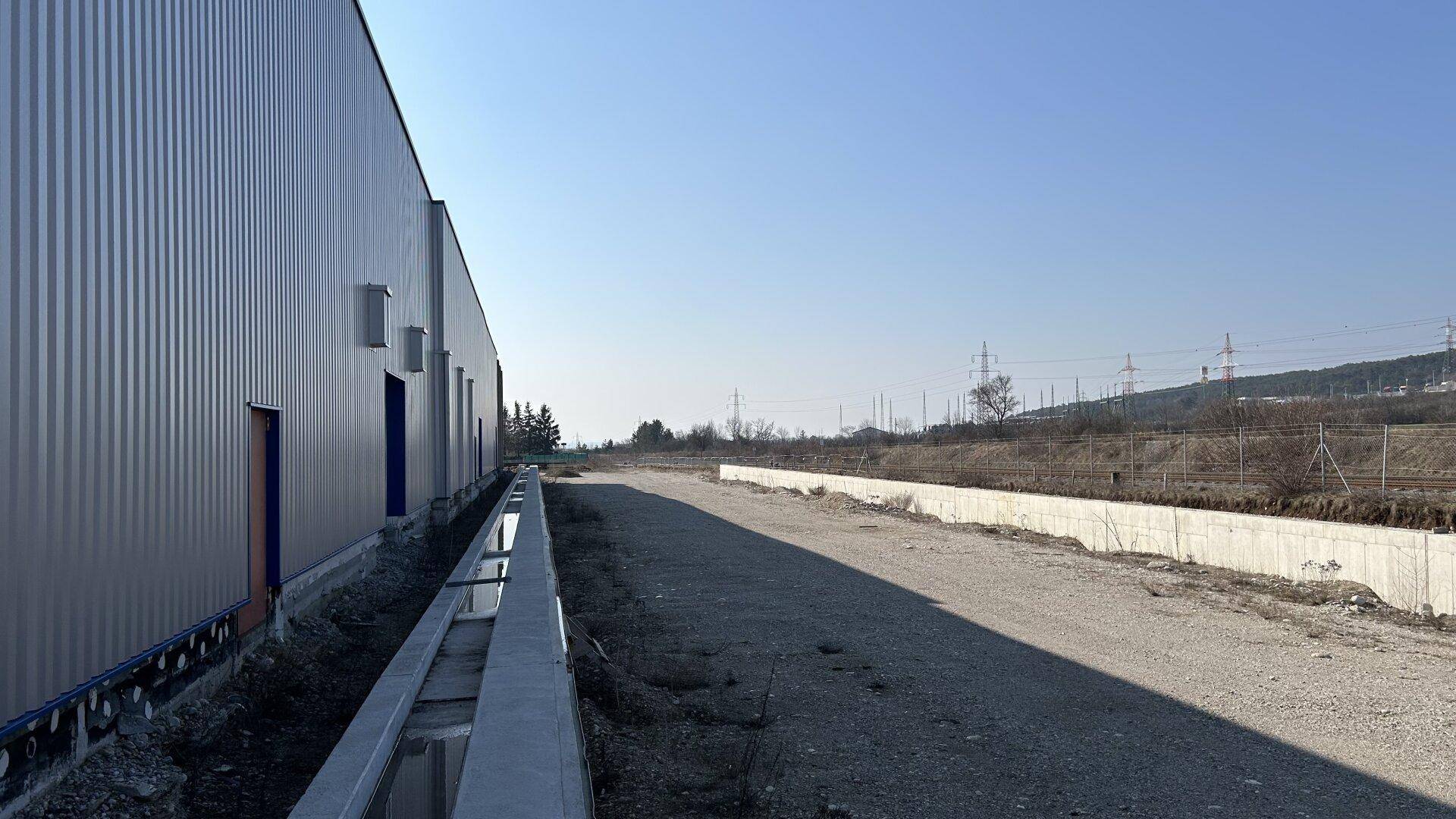 Lange Seitenansicht des Industriegebäudes mit Entwässerungsgraben und weitem Blick in die Landschaft.