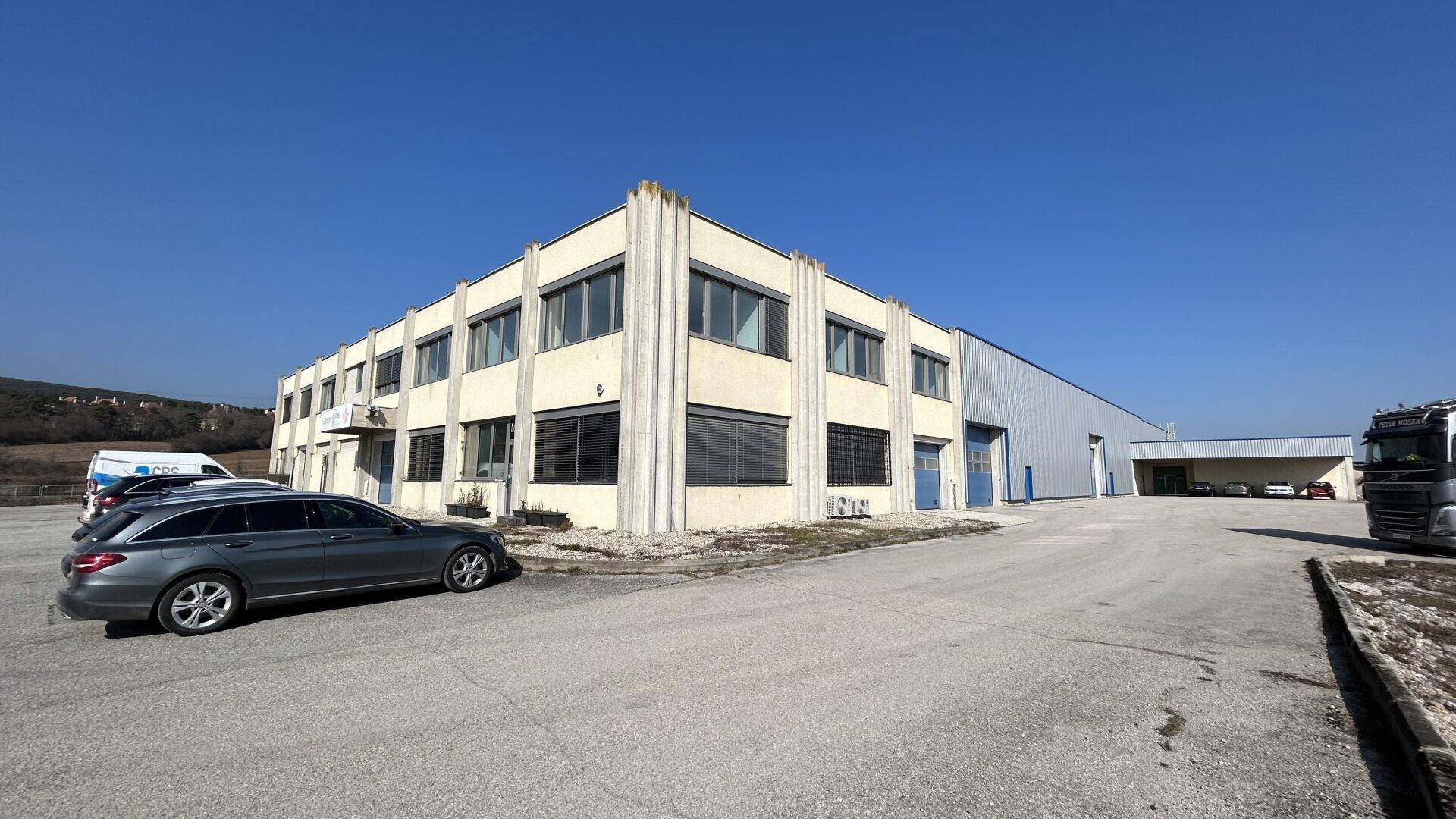 Weitläufige Ansicht des Industriegebäudes mit Parkplätzen und Zufahrt unter klarem Himmel.