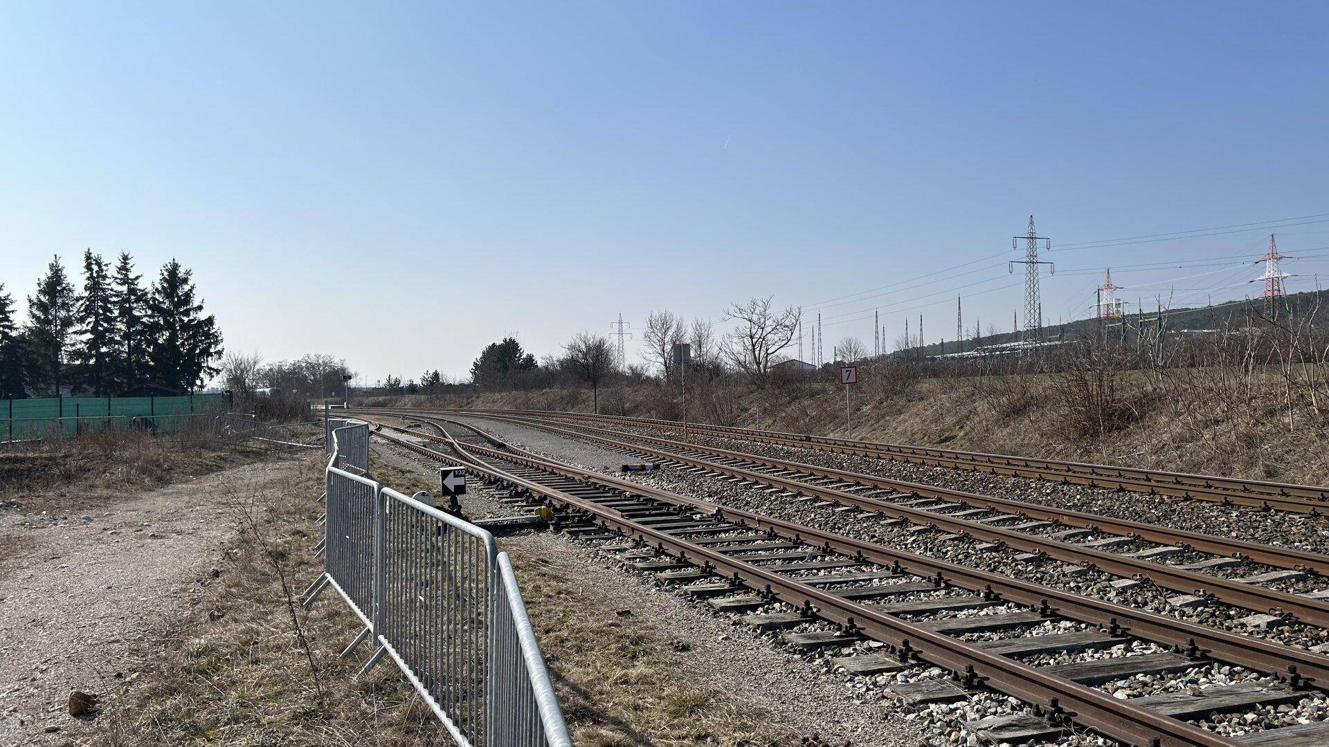 Bahngleise verlaufen entlang des Grundstücks, umgeben von Vegetation und Stromleitungen in der Ferne.