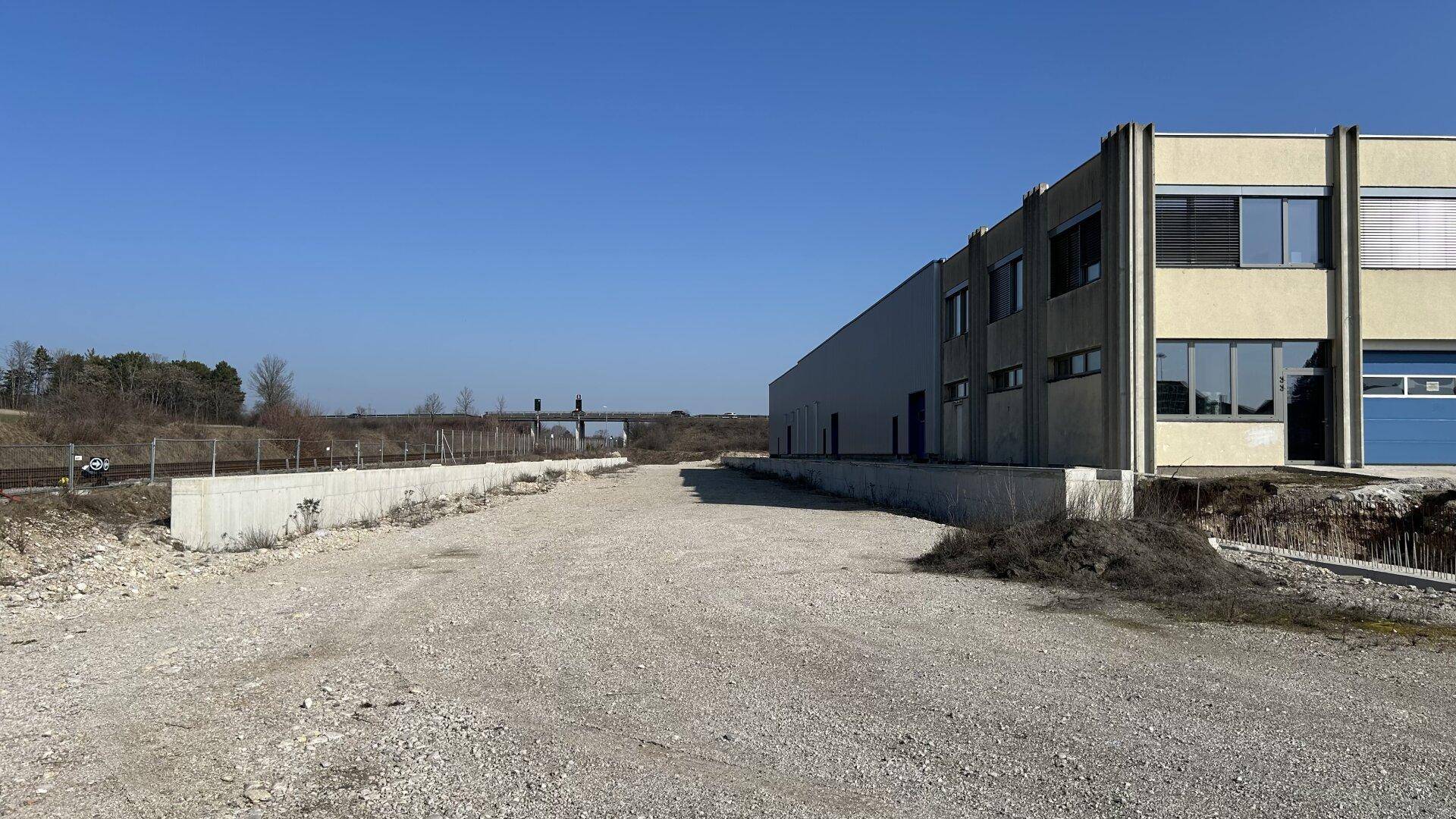 Seitenansicht des Industriegebäudes mit angrenzendem Freigelände und Bahngleisen im Hintergrund.