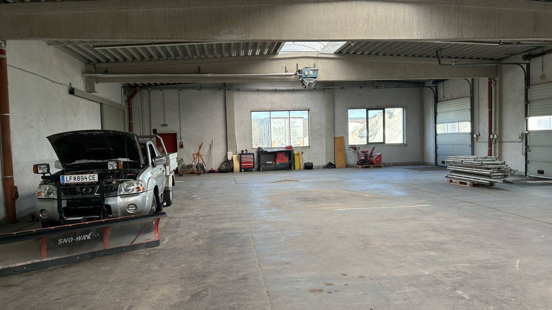 Werkstattbereich mit einem Fahrzeug auf einer Hebebühne und Rolltoren im Hintergrund.
