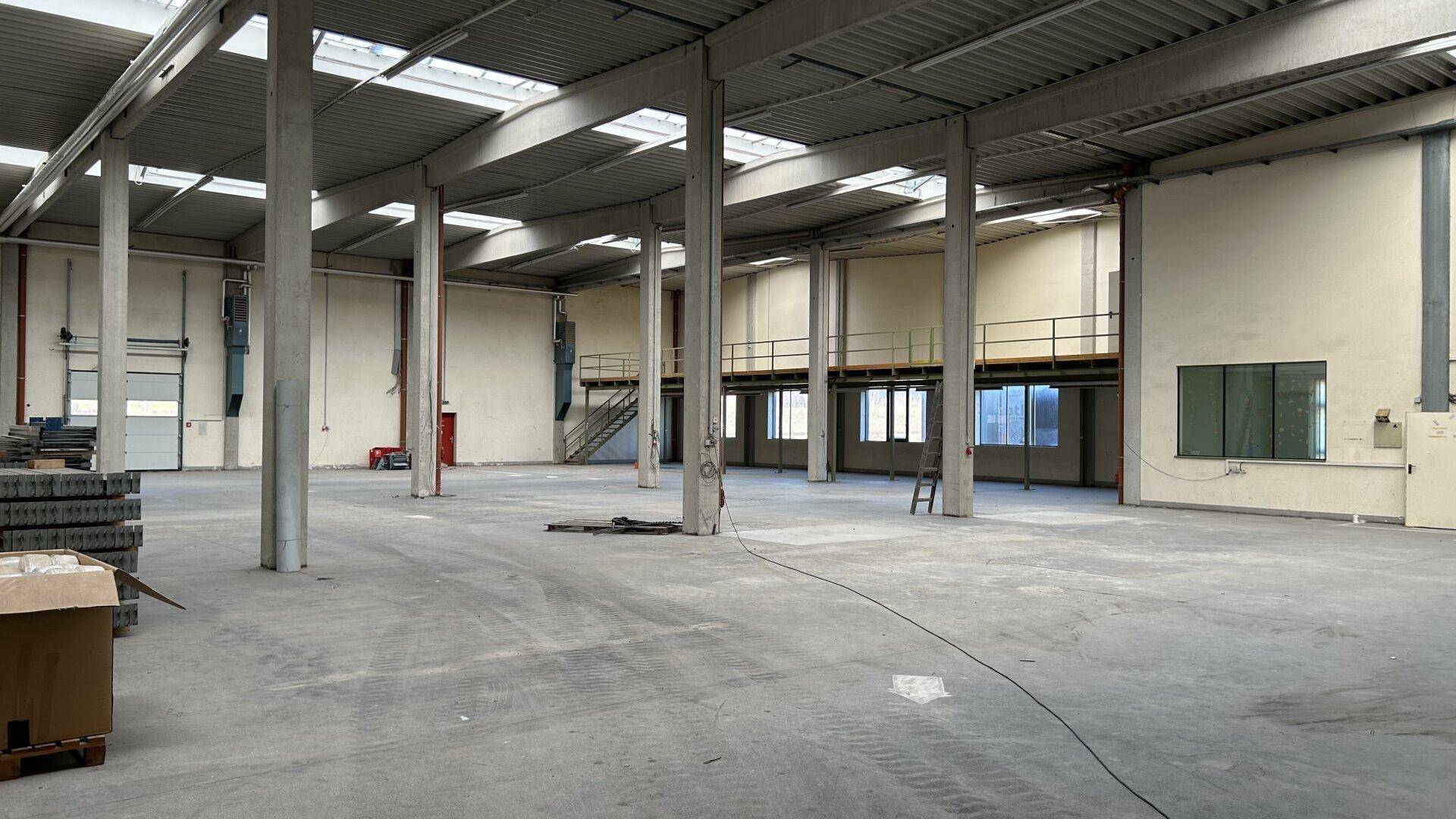 Geräumige Lagerhalle mit hohen Decken, Betonboden und Oberlichtern für natürliches Licht.