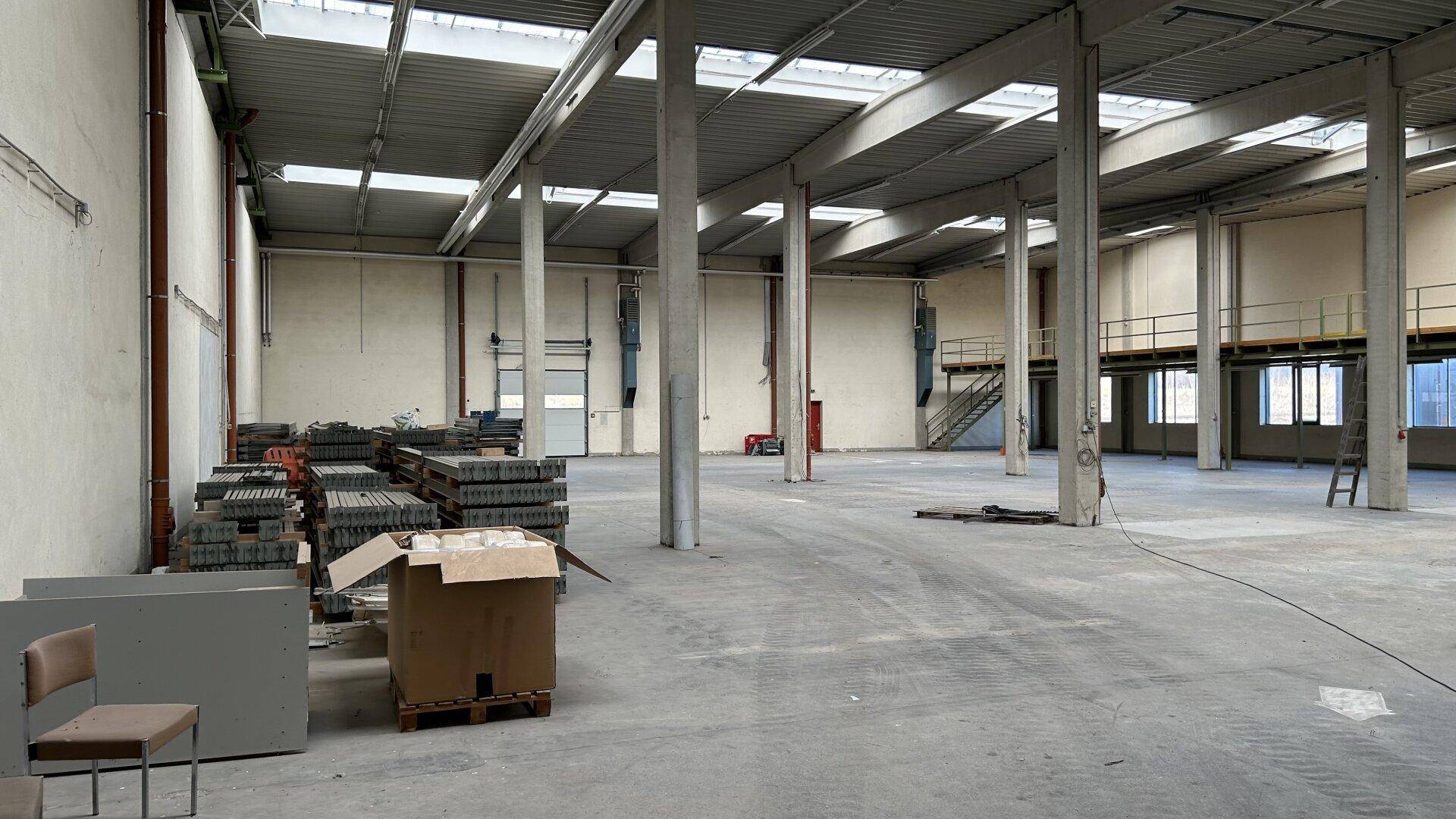 Geräumige Lagerhalle mit hohen Decken, Betonboden und Oberlichtern für natürliches Licht.