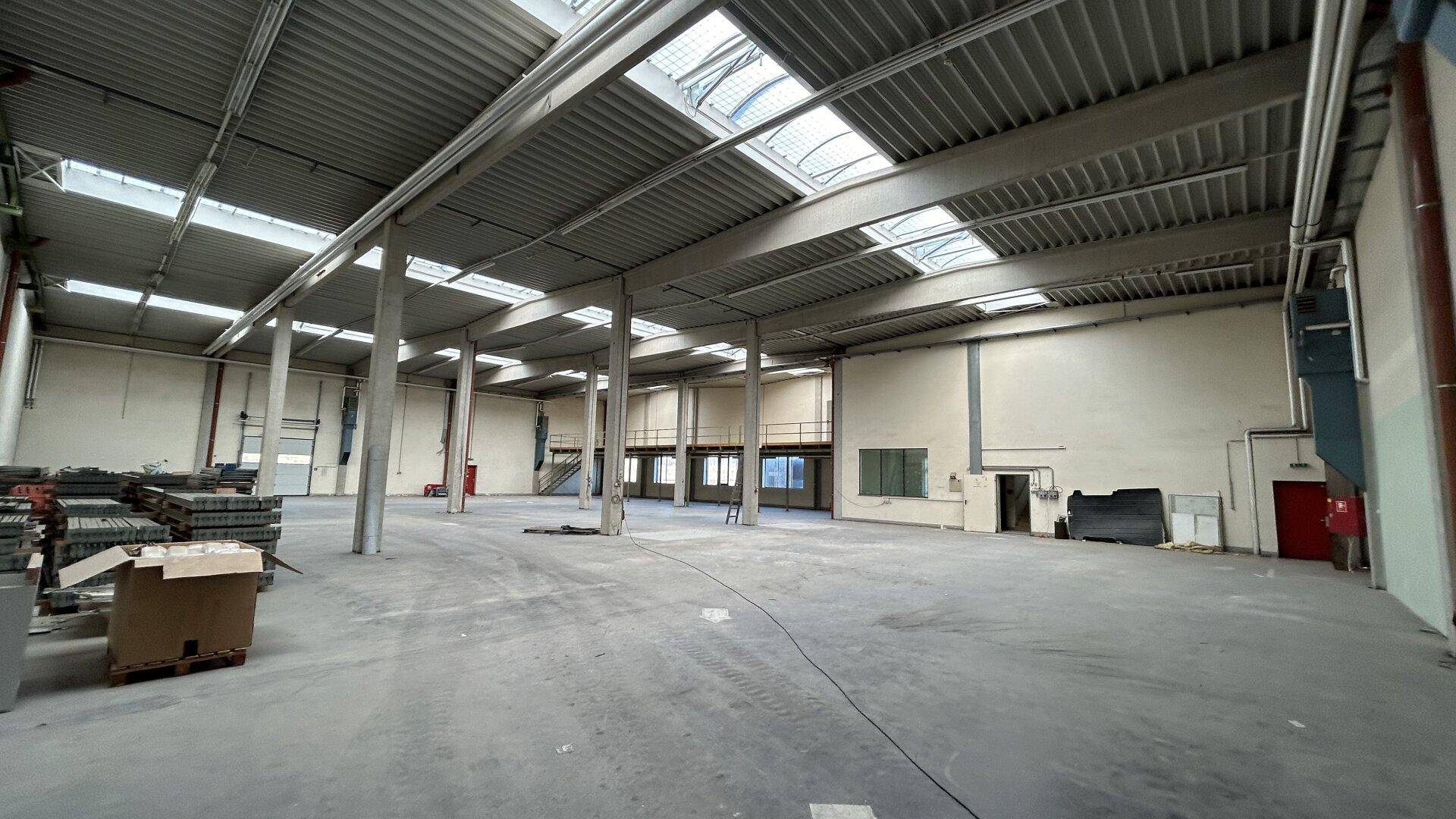 Geräumige Lagerhalle mit hohen Decken, Betonboden und Oberlichtern für natürliches Licht.