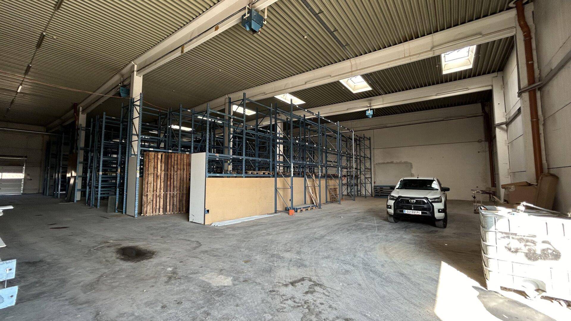 Lagerhalle mit hohen Regalen, Paletten und einem geparkten Fahrzeug auf dem Betonboden.