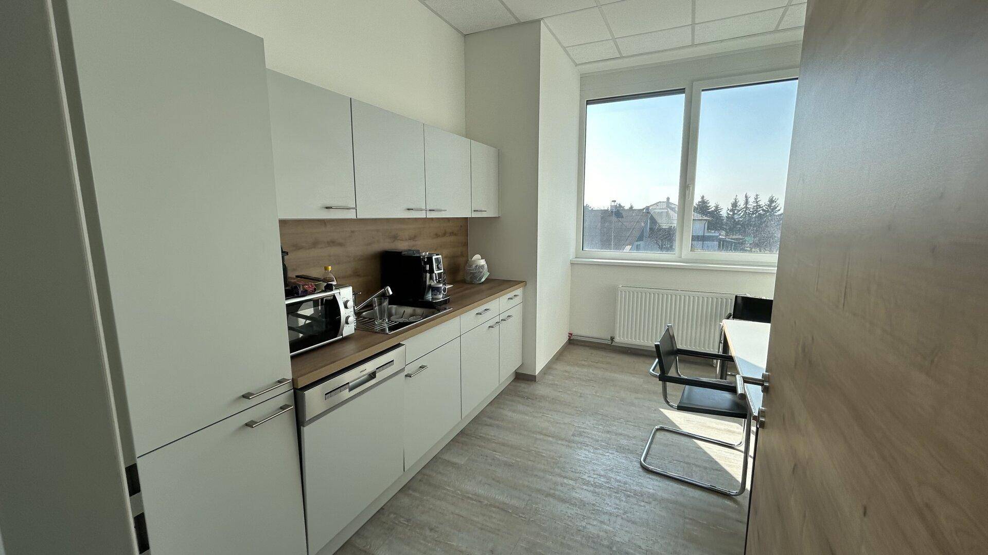 Moderne Teeküche mit weißen Schränken, Holzarbeitsplatte und Fenster, ideal für Pausen.