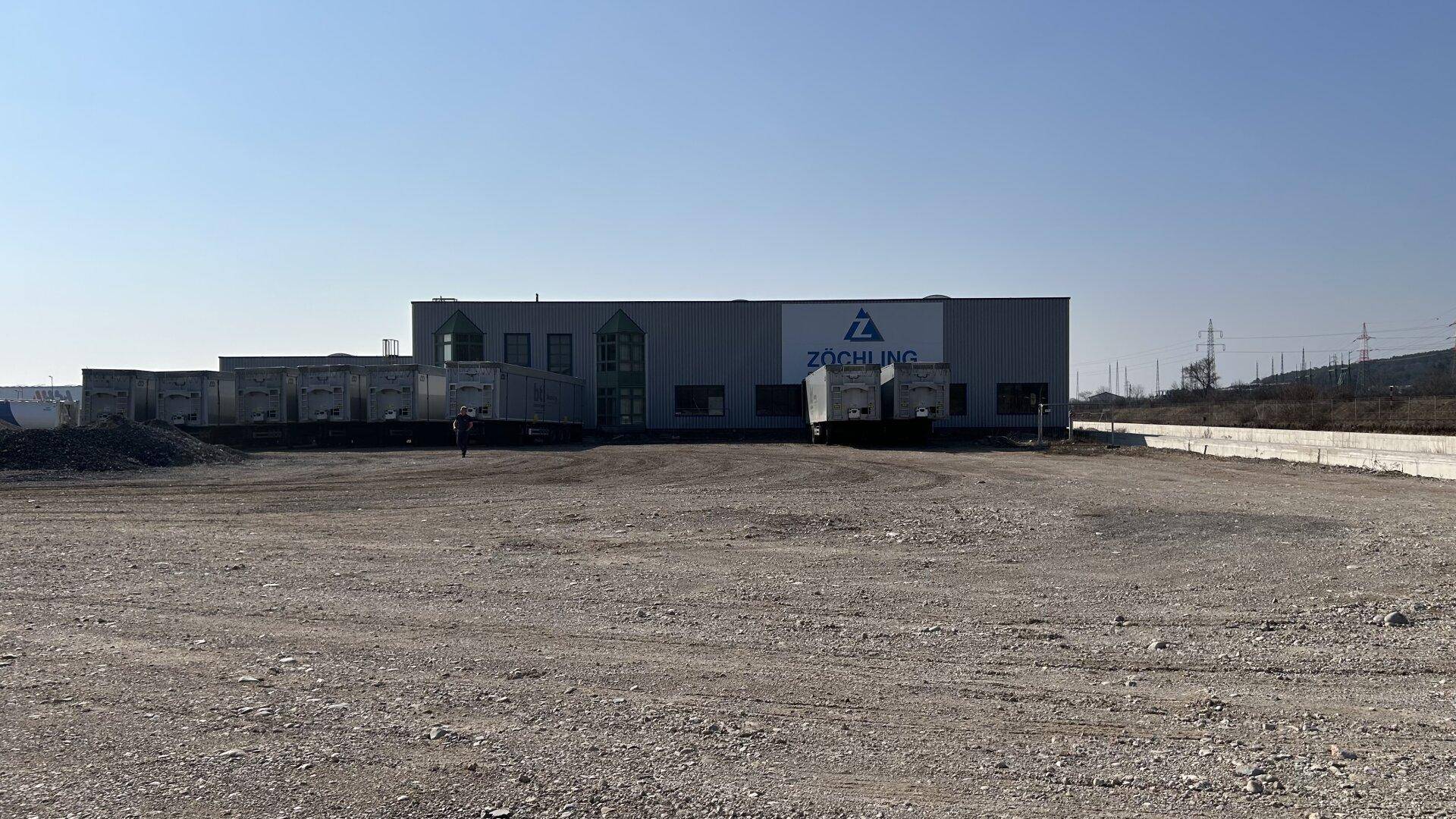 Modernes Industriegebäude mit Firmenlogo und Laderampen auf einem weitläufigen Gelände.