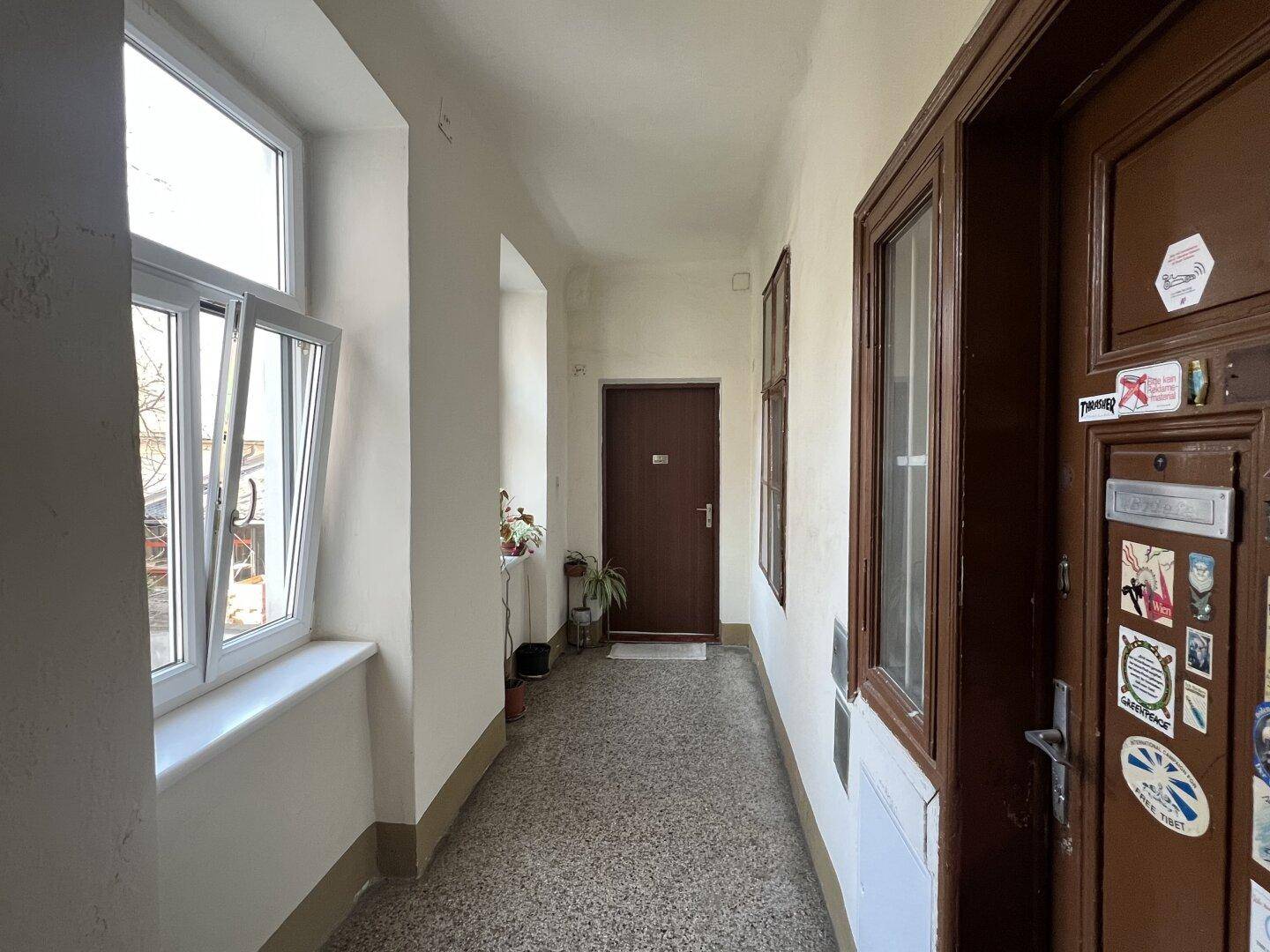Langer Flur in einem Altbau mit Terrazzoboden, braunen Holztüren und einem geöffneten Fenster.