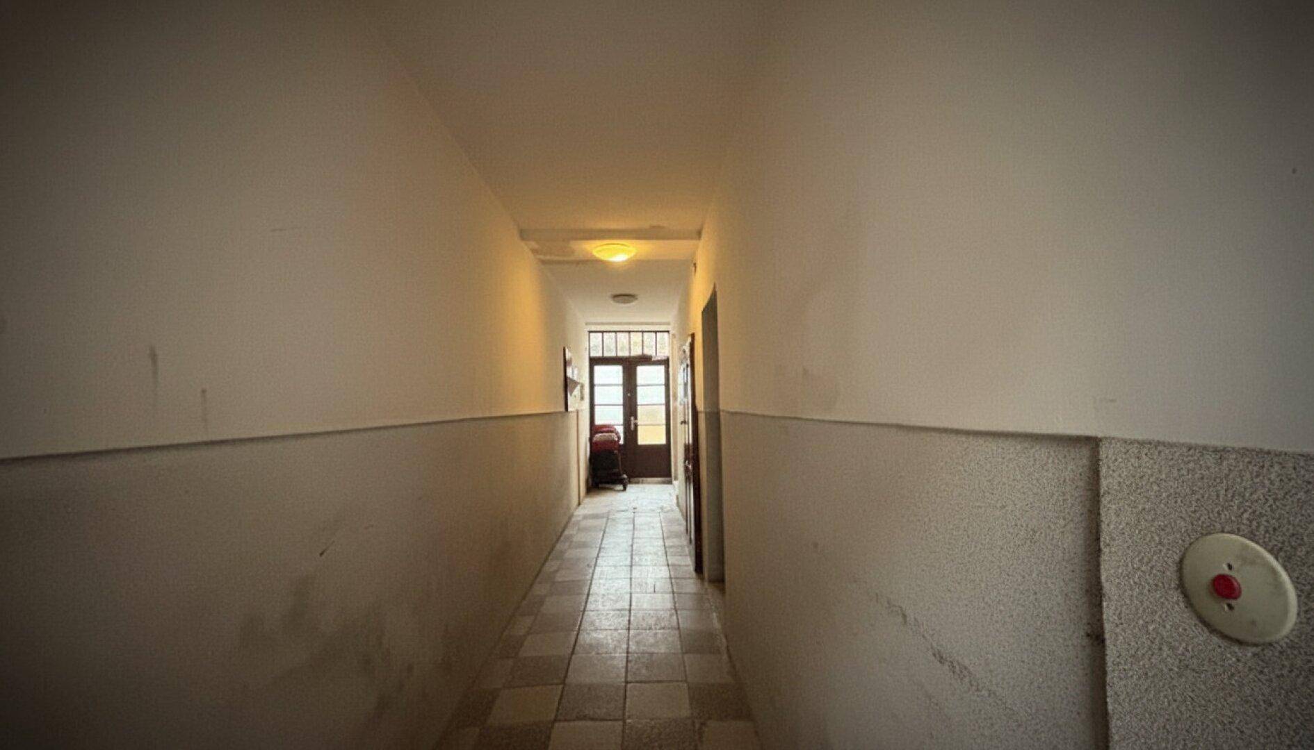 Langer, schmaler Flur mit Fliesenboden und einer Tür am Ende.