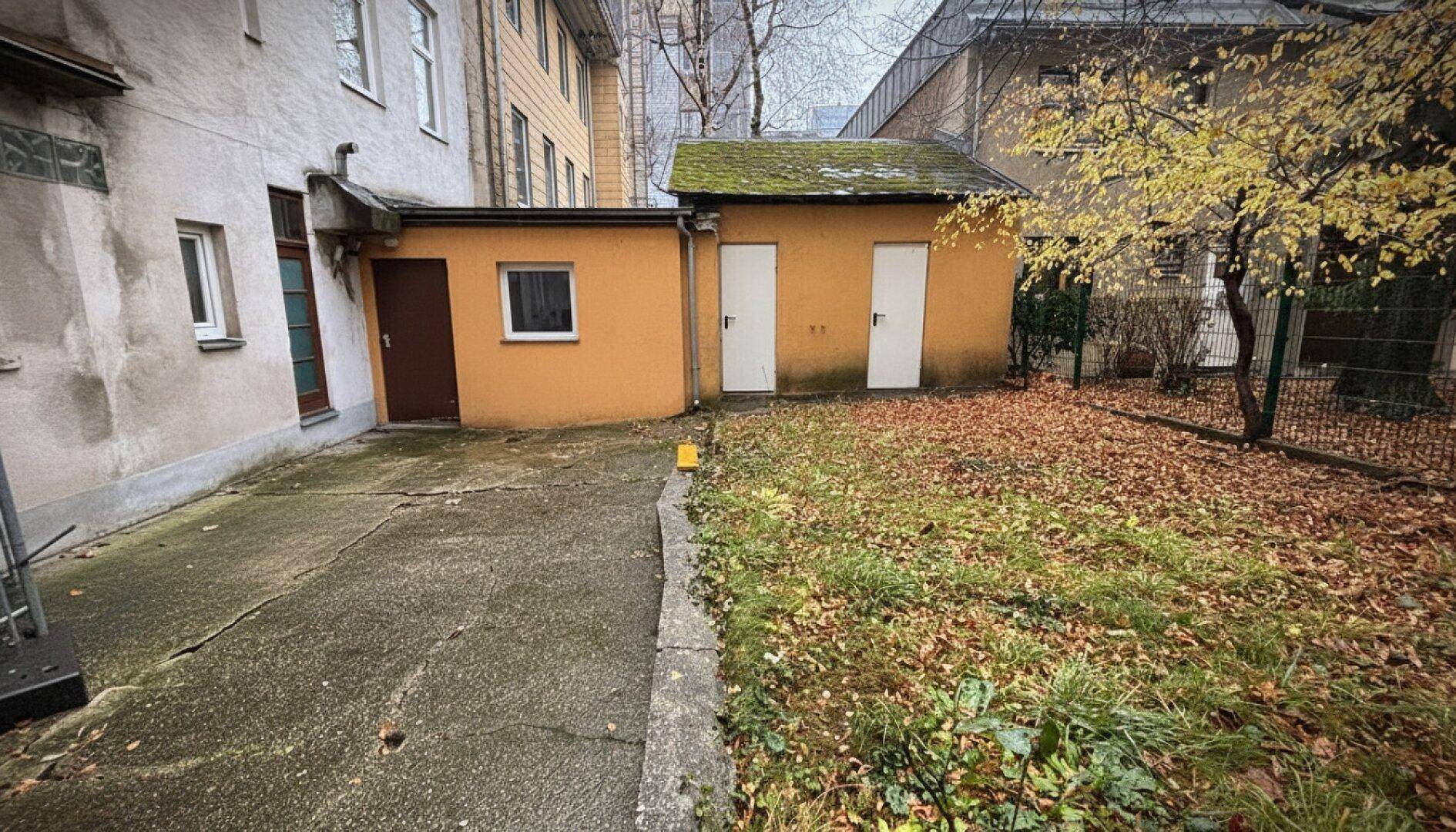 Hinterhof mit Rasenfläche, kleinen Gebäuden und herbstlichem Laub.