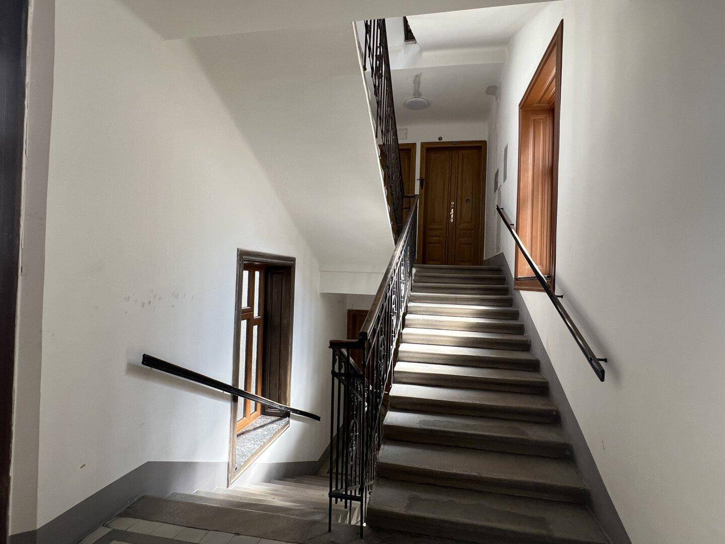 Historisches Treppenhaus mit schmiedeeisernem Geländer, Holzstufen und hohen Decken in gutem Zustand.