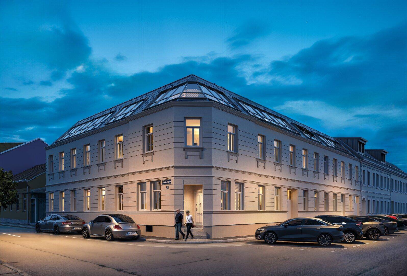 Beleuchtetes Eckgebäude bei Nacht mit moderner Architektur und Parkplätzen.