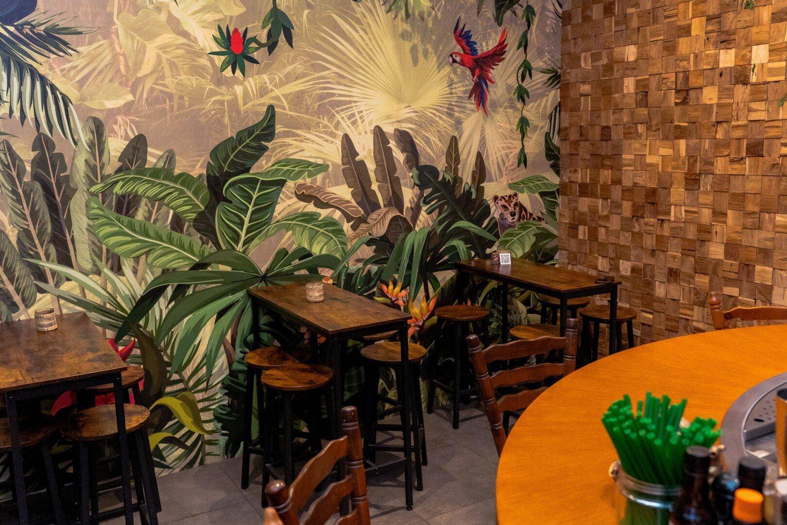 Ein lebhafter Restaurantbereich mit Dschungel-Wandtapete, Holztischen und Hockern, die eine exotische Atmosphäre schaffen.