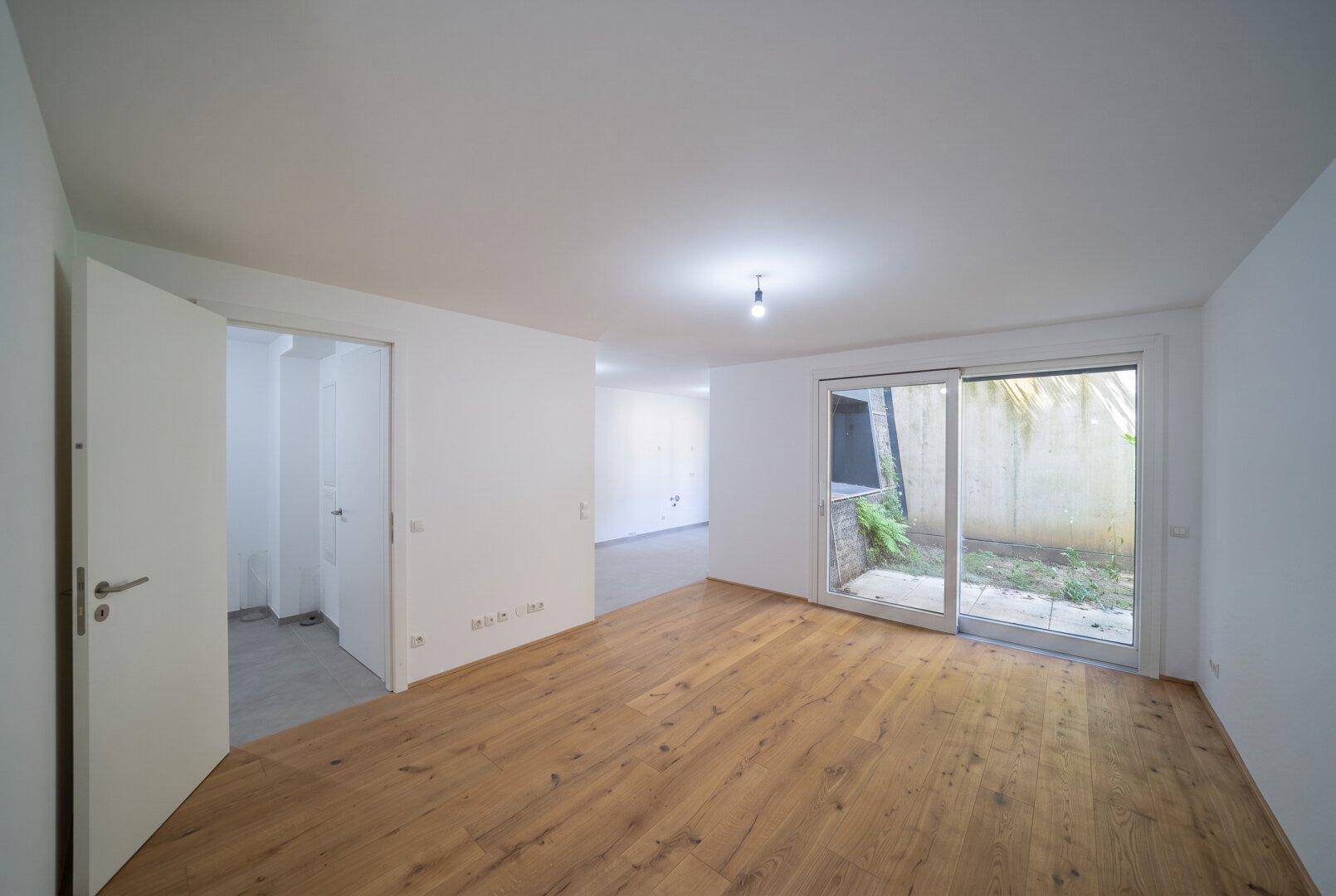 Geräumiges Wohnzimmer mit Holzboden und Schiebetür zum Außenbereich, offen zu weiteren Räumen.
