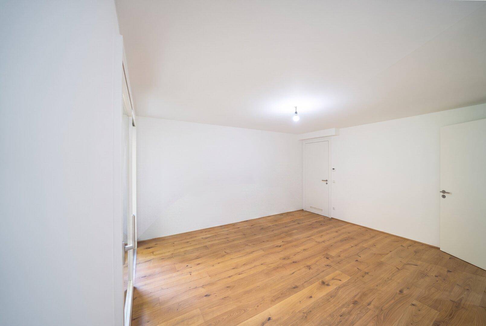 Leeres Schlafzimmer mit hellem Holzboden und weißen Wänden, bereit zur individuellen Gestaltung.