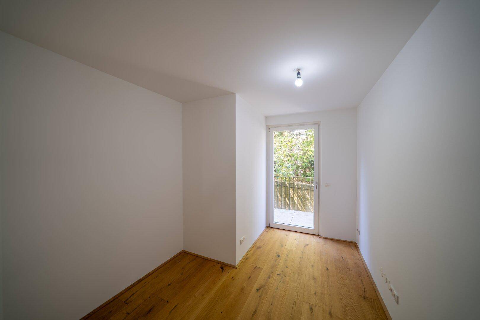 Kleines helles Zimmer mit Holzboden und Zugang zu einem Balkon.