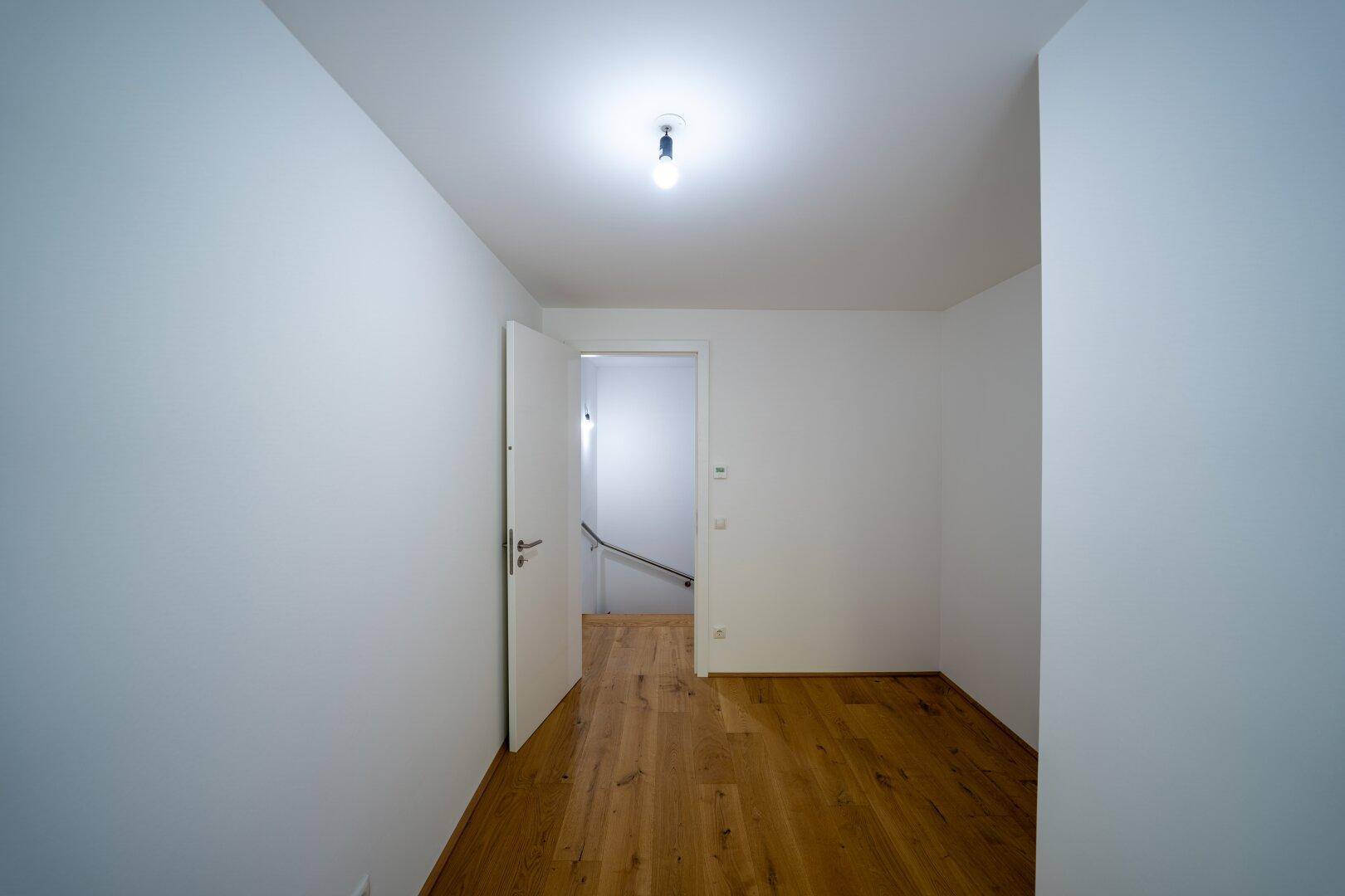 Heller Raum mit Holzboden und offenem Zugang zu einem Treppenhaus.